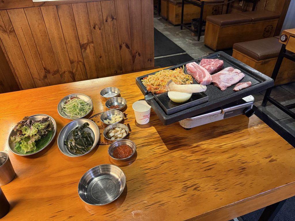焼く前の豚肉と、サンチュやニンニクなどのおかずが並んだテーブル